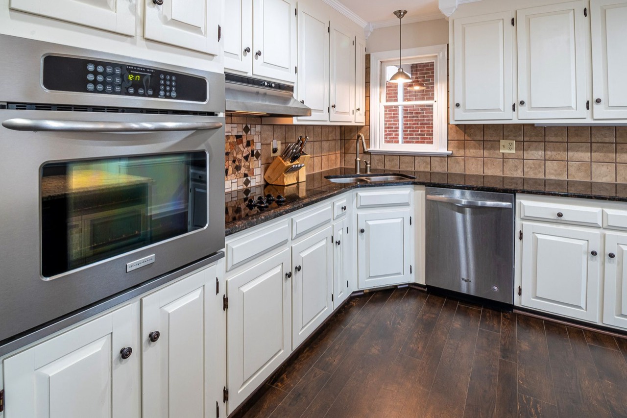 Kitchen with white raised-panel cabinets, a built-in oven and dark wood flooring