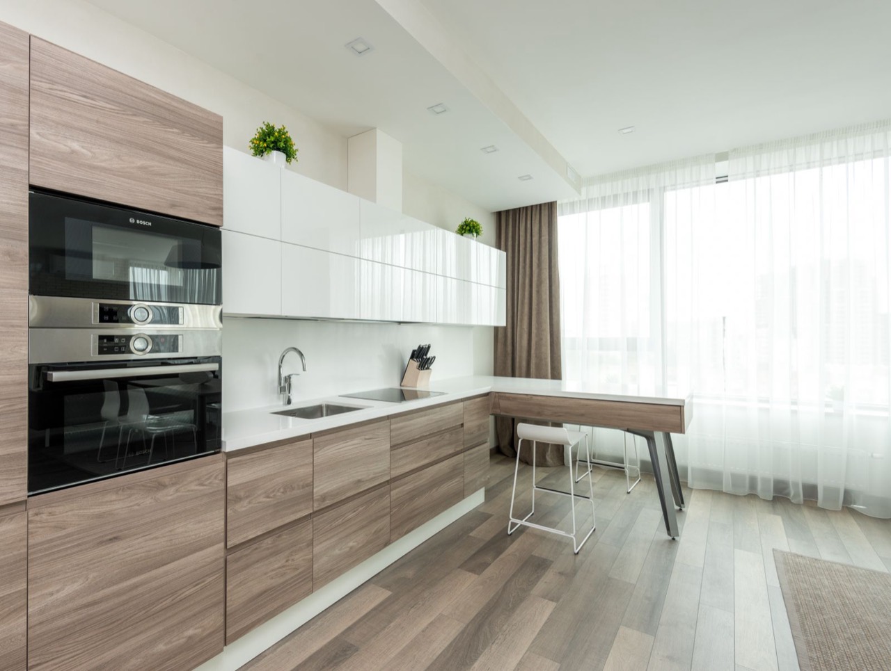 Bright kitchen with wood-grain lower cabinets, glossy white upper cabinets and built-in ovens